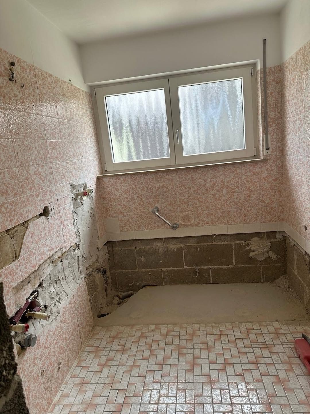 Bad vor der Sanierung — alte Fliesen, ausgebaute Wanne, freigelegte Rohrleitungen